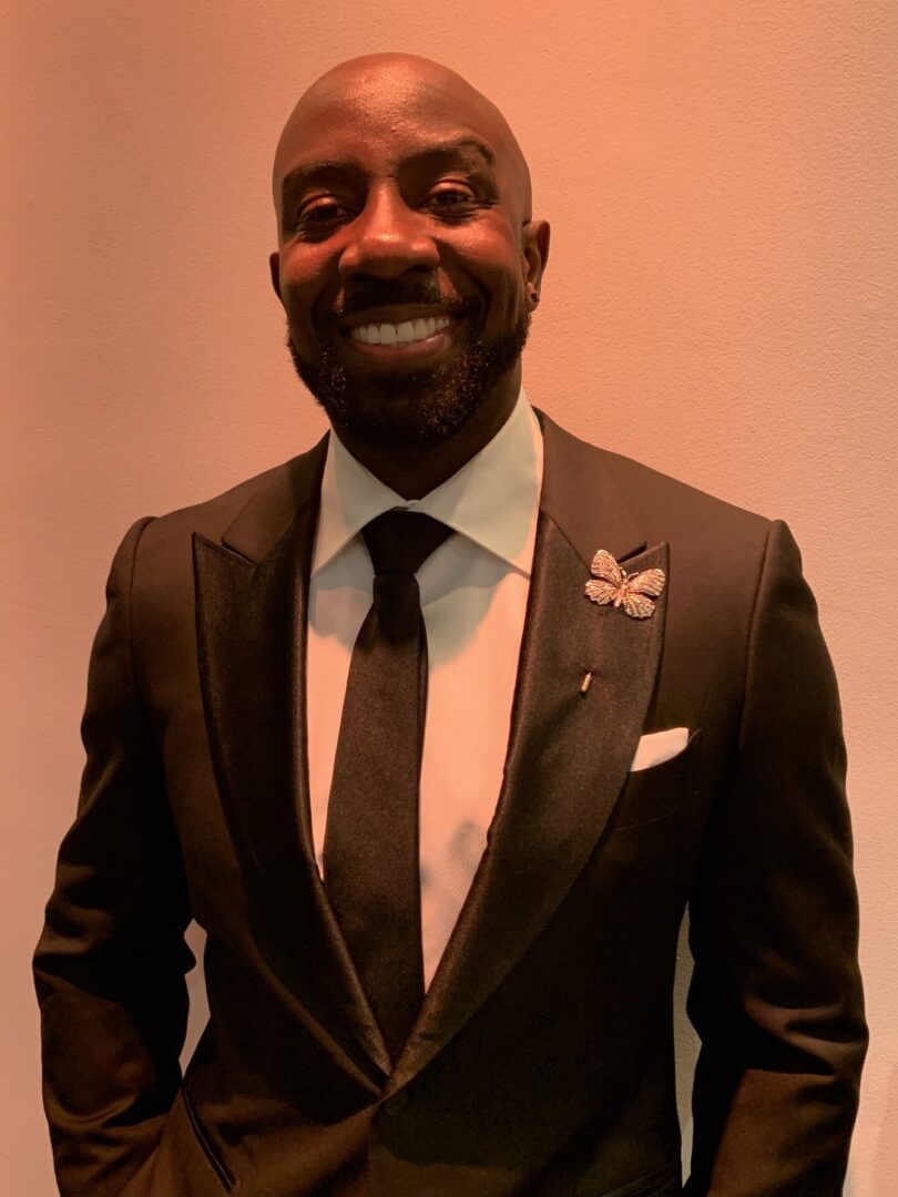 A black man in a tuxedo smiling for the camera during a consultation at Beauchamp Consulting.