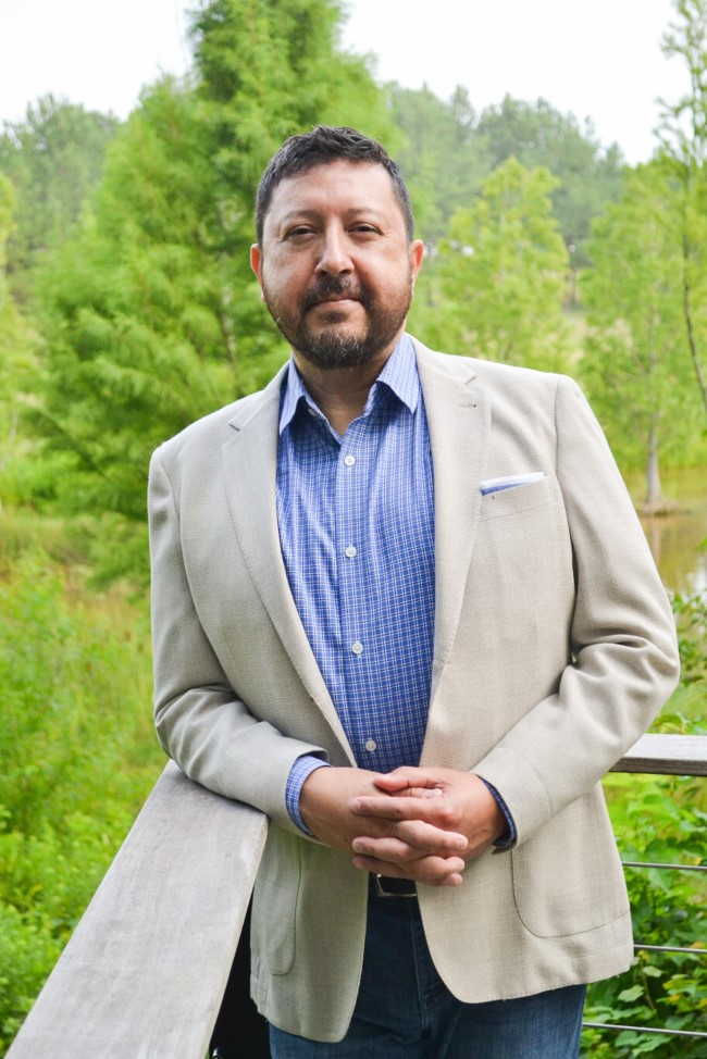 A man in a blazer standing on a wooden railing. Beauchamp Consulting offers customized support to help you achieve your goals.